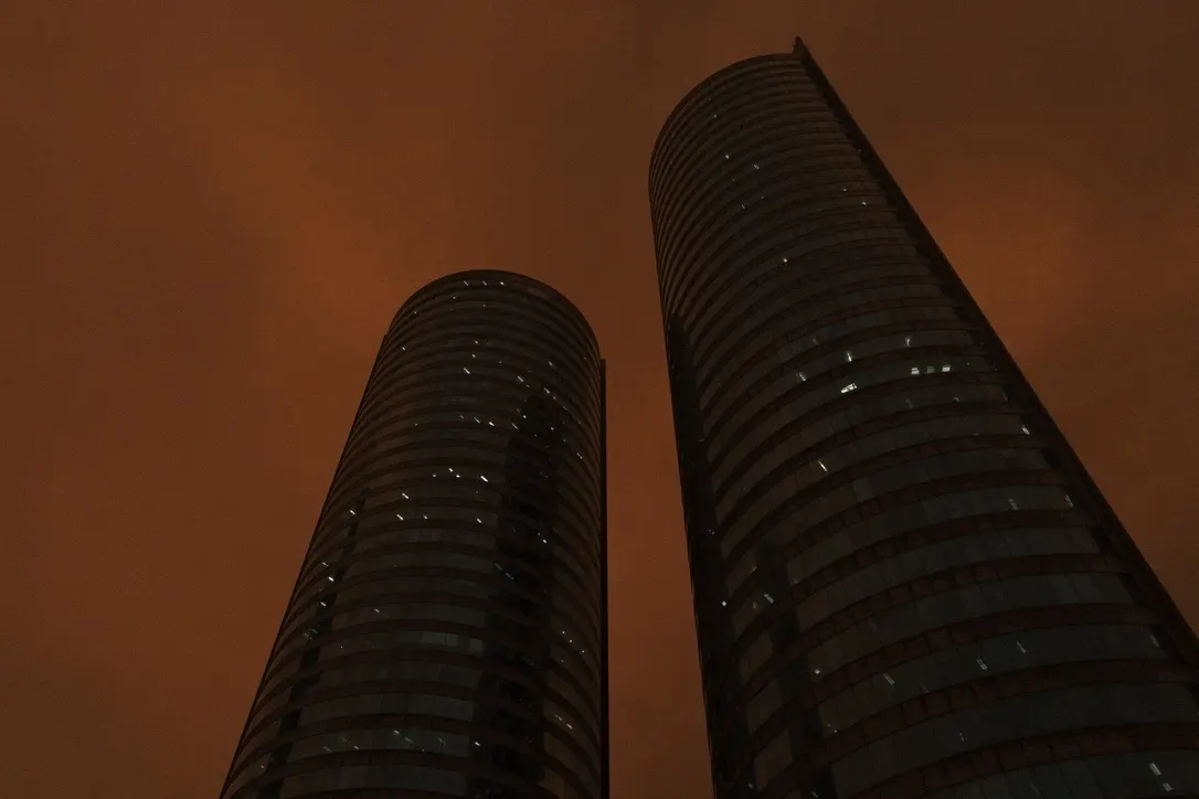 Two cylindrical glass towers seen from below against an amber sky