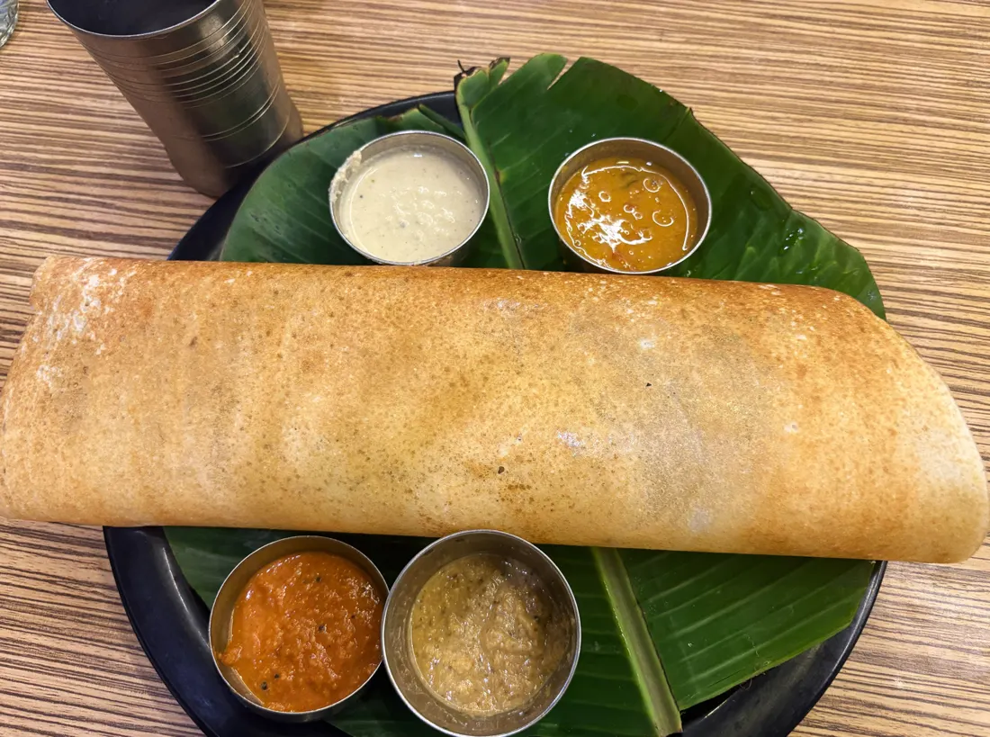 A masala dosa on a banana leaf with chutneys and sambar