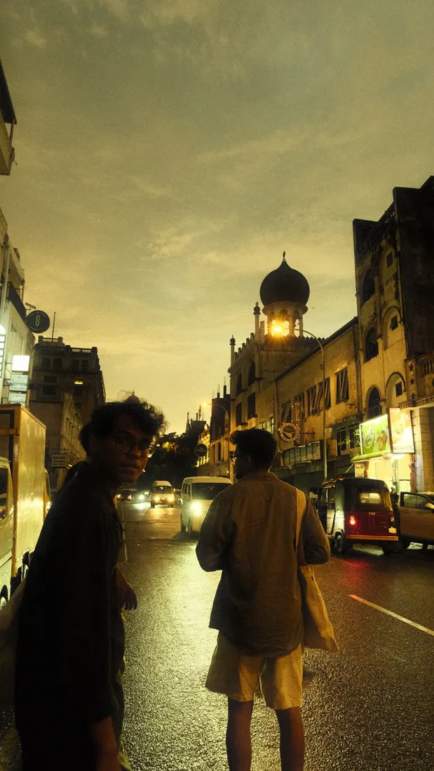 Friends walking down a wet street at dusk, a mosque dome lit behind them