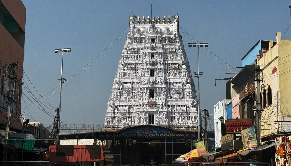 A tall carved white temple gopuram above a busy street